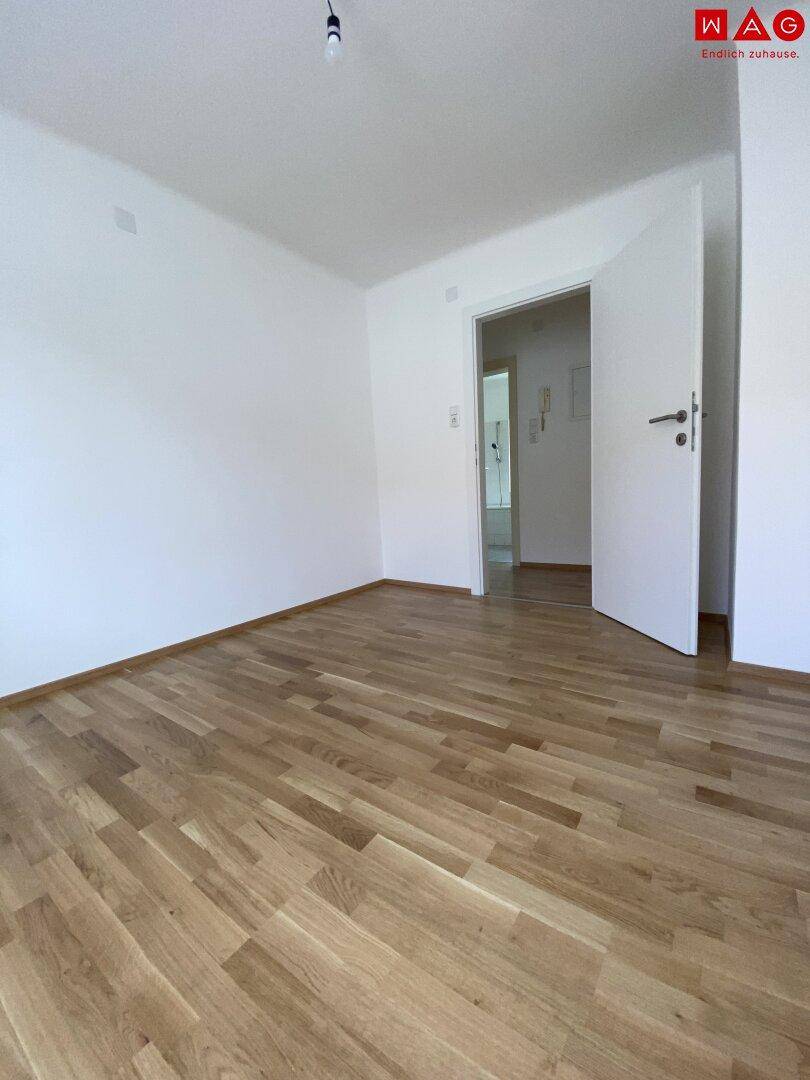Helles Schlafzimmer mit Parkettboden und Zugang zu einem weiteren Raum.