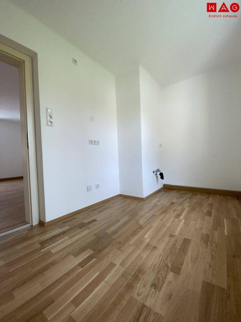 Leerer Küchenraum mit Anschlüssen für eine zukünftige Einbauküche und Parkettboden.