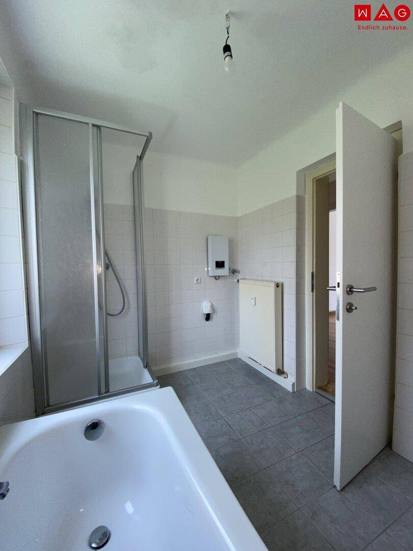 Helles Badezimmer mit Badewanne, Duschkabine und Fliesenboden in neutralen Farben.