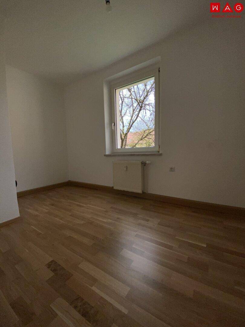 Schlafzimmer mit Parkettboden und einem Fenster, das den Blick nach draußen freigibt.