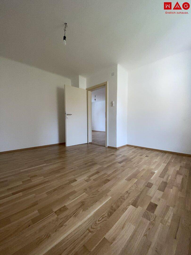 Helles Schlafzimmer mit Parkettboden und Zugang zu einem angrenzenden Bereich.