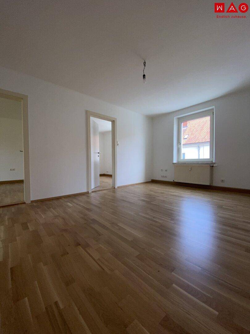 Geräumiges Wohnzimmer mit Parkettboden und einem Fenster, das Tageslicht hereinlässt.