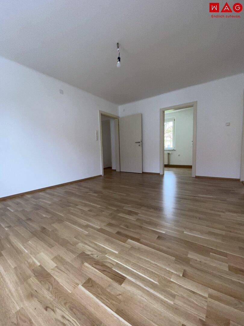 Heller Wohnbereich mit Parkettboden und Zugang zu angrenzenden Räumen.