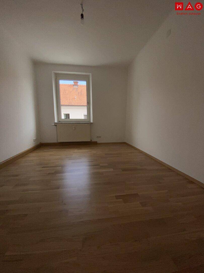 Geräumiges Schlafzimmer mit Parkettboden und einem Fenster mit Blick auf das Dach.