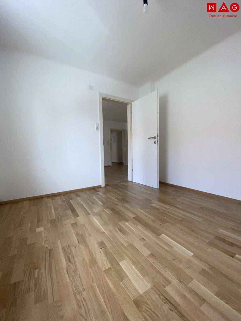 Helles Schlafzimmer mit Parkettboden und weiß gestrichenen Wänden, ideal für individuelle Gestaltung.