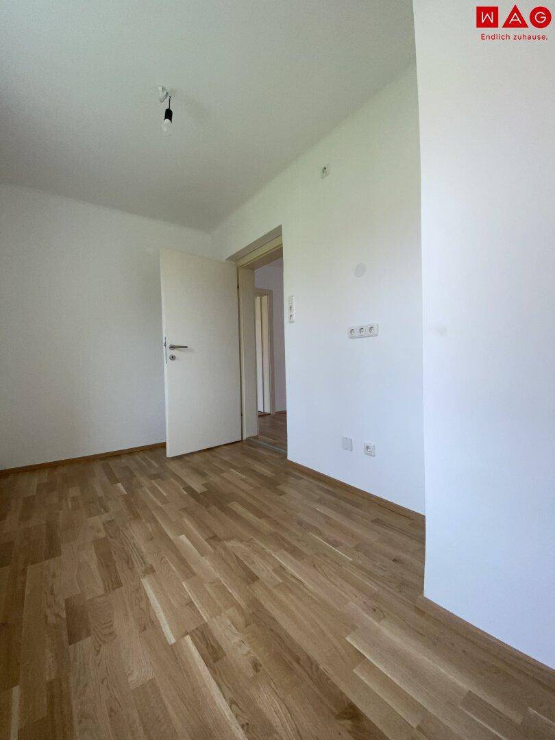 Helles Schlafzimmer mit Parkettboden und weiß gestrichenen Wänden, bereit zur Einrichtung.