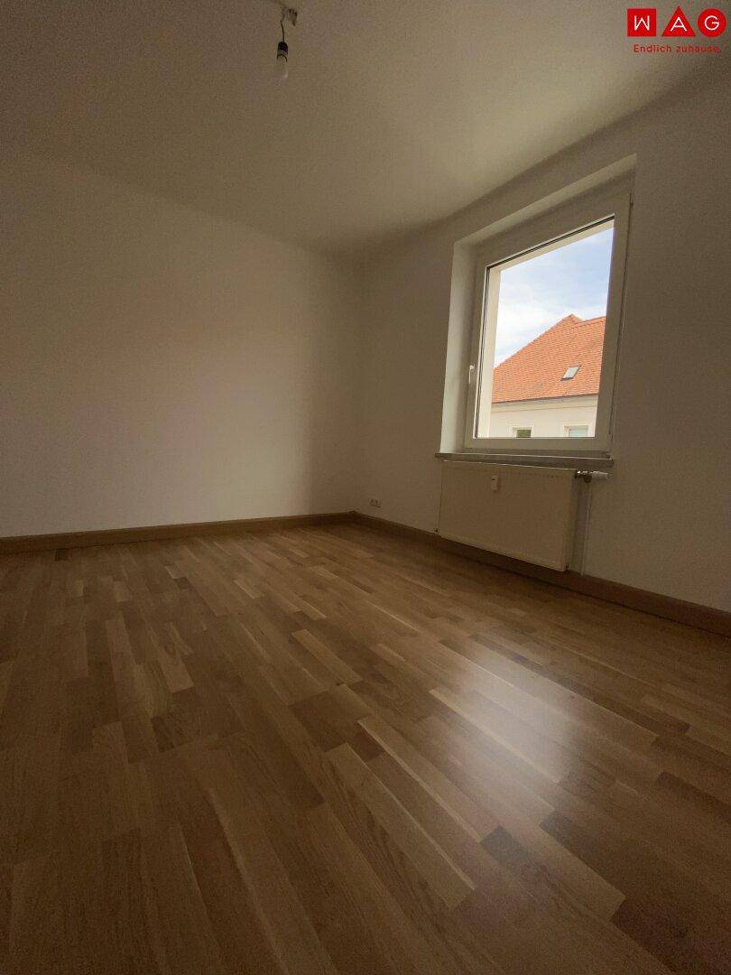 Schlafzimmer mit Parkettboden und einem Fenster, das viel Tageslicht spendet.