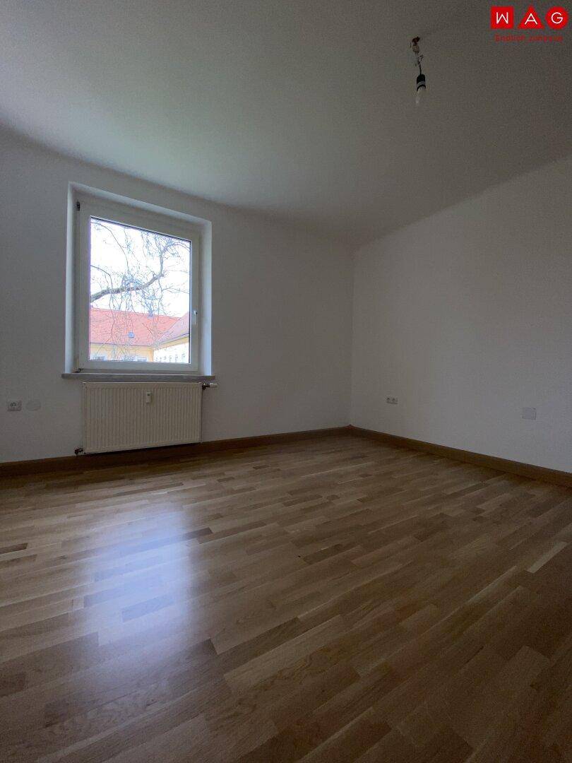 Geräumiges Schlafzimmer mit Parkettboden und einem Fenster, das den Raum erhellt.