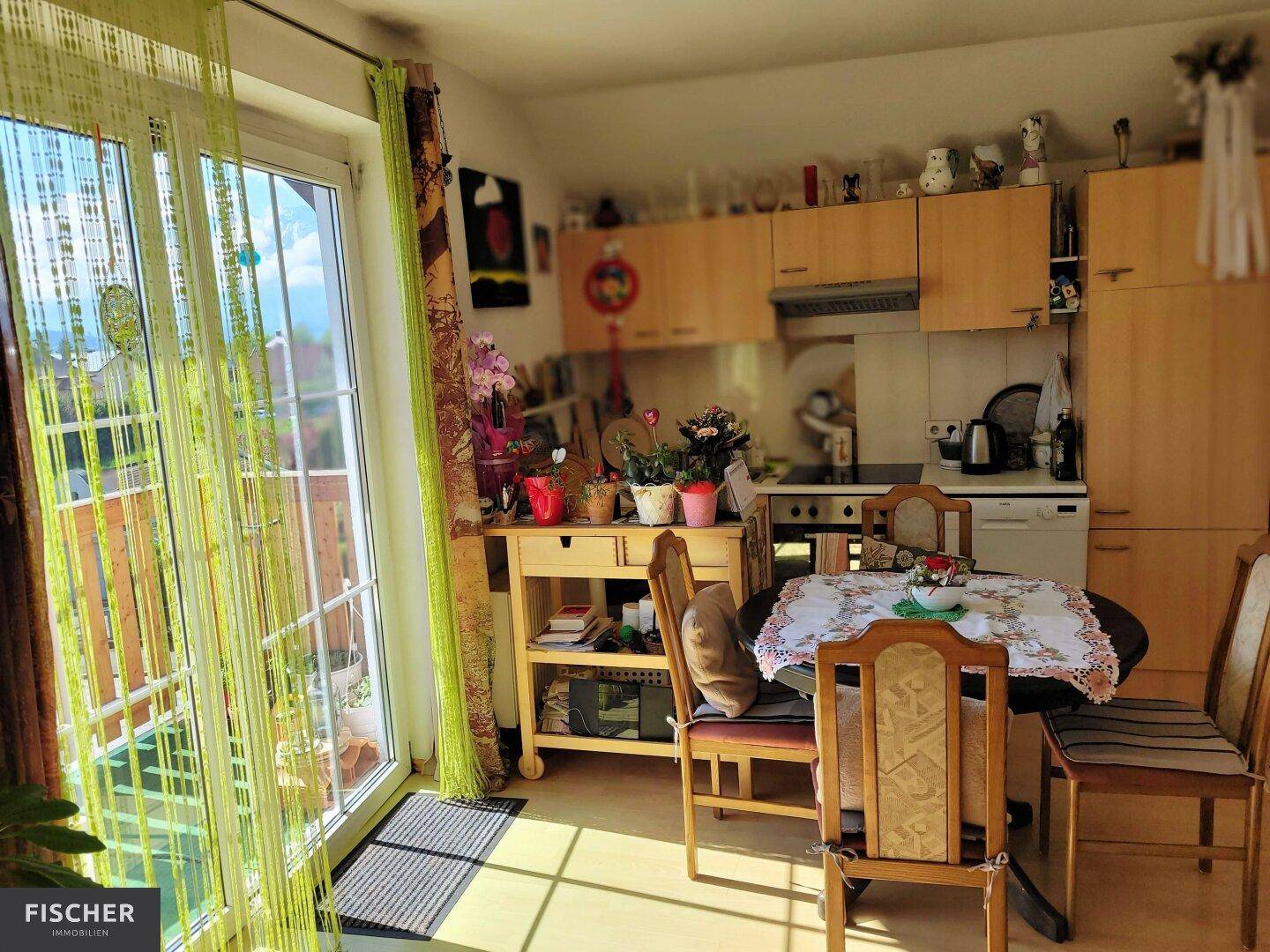 Helle Wohnküche mit Holzschränken, Essbereich und direktem Zugang zum Balkon.