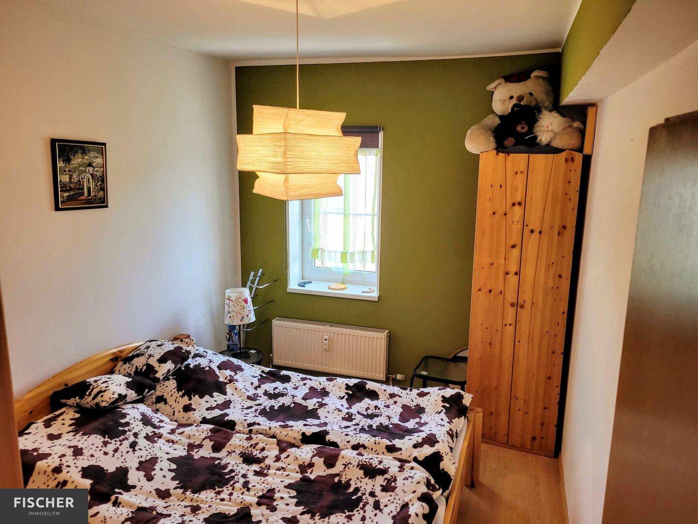 Schlafzimmer mit Doppelbett, Holzschrank und grüner Akzentwand.