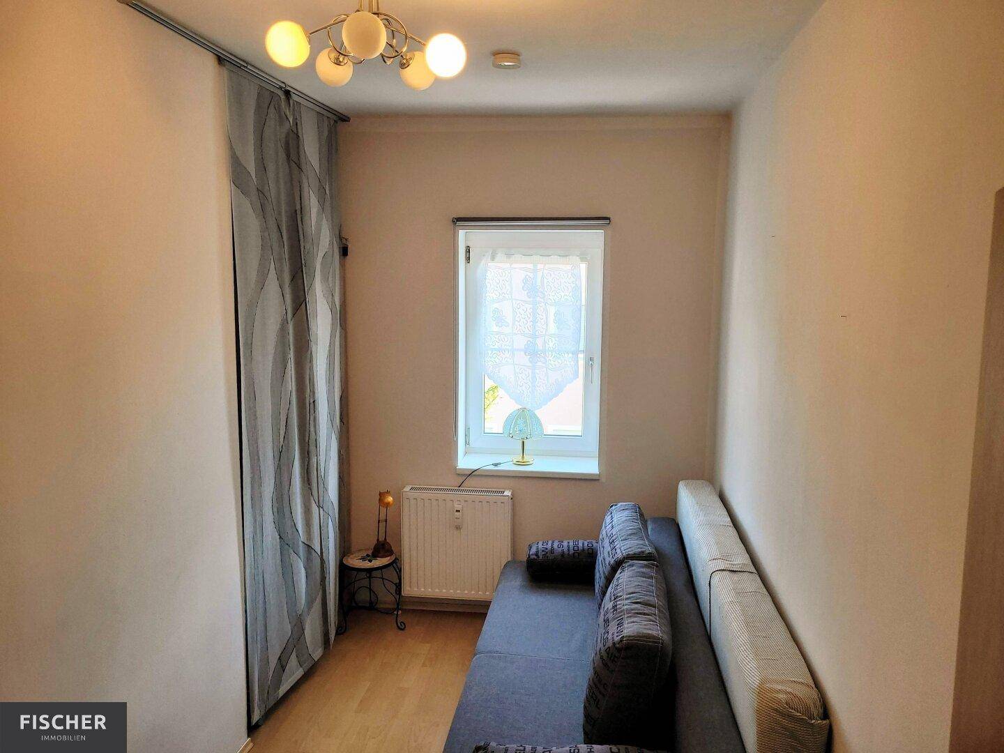 Kleines Zimmer mit Schlafsofa, Parkettboden und Fenster.