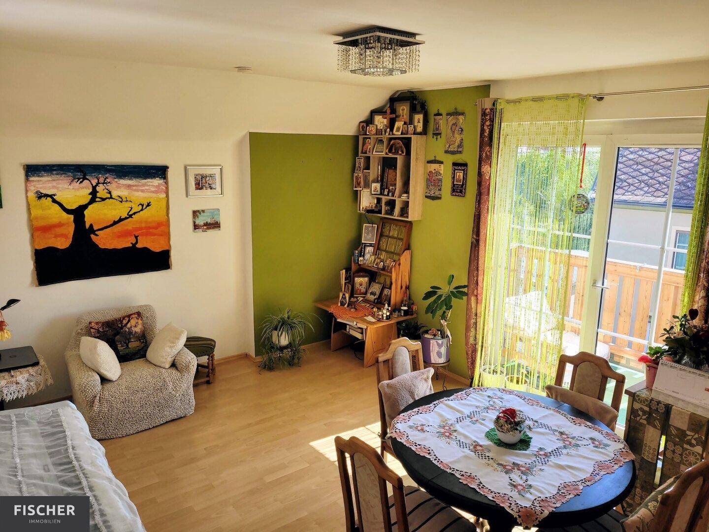 Gemütlicher Wohnbereich mit Parkettboden, grüner Akzentwand und Zugang zum Balkon.