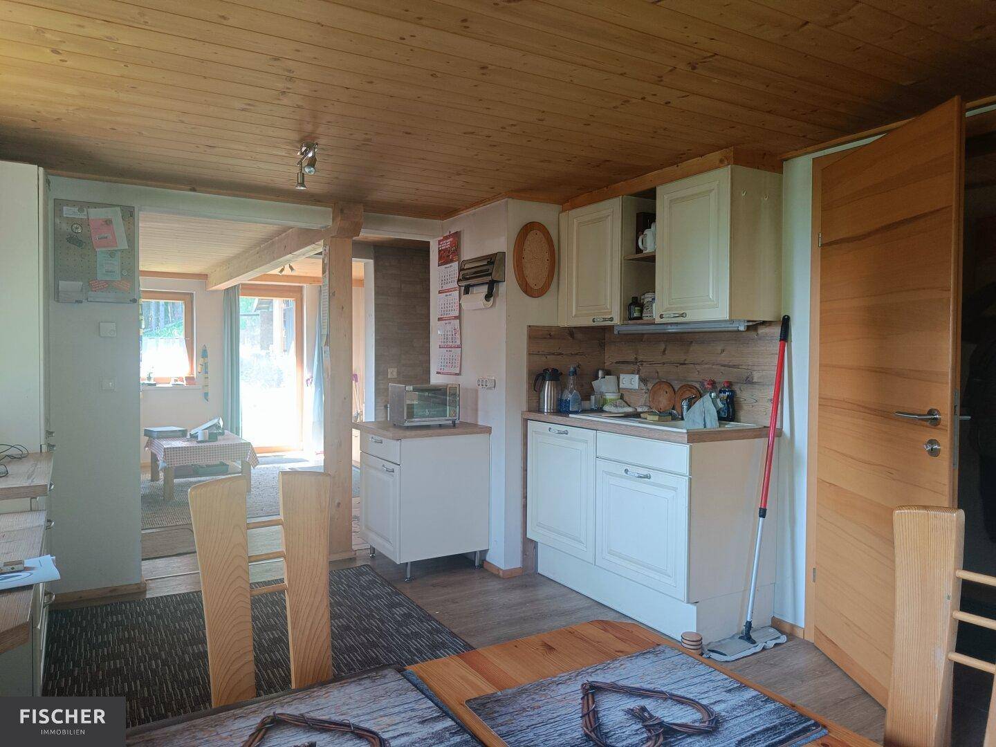 Offener Küchenbereich mit Holzakzenten und Blick in den angrenzenden Wohnraum mit Zugang nach draußen.