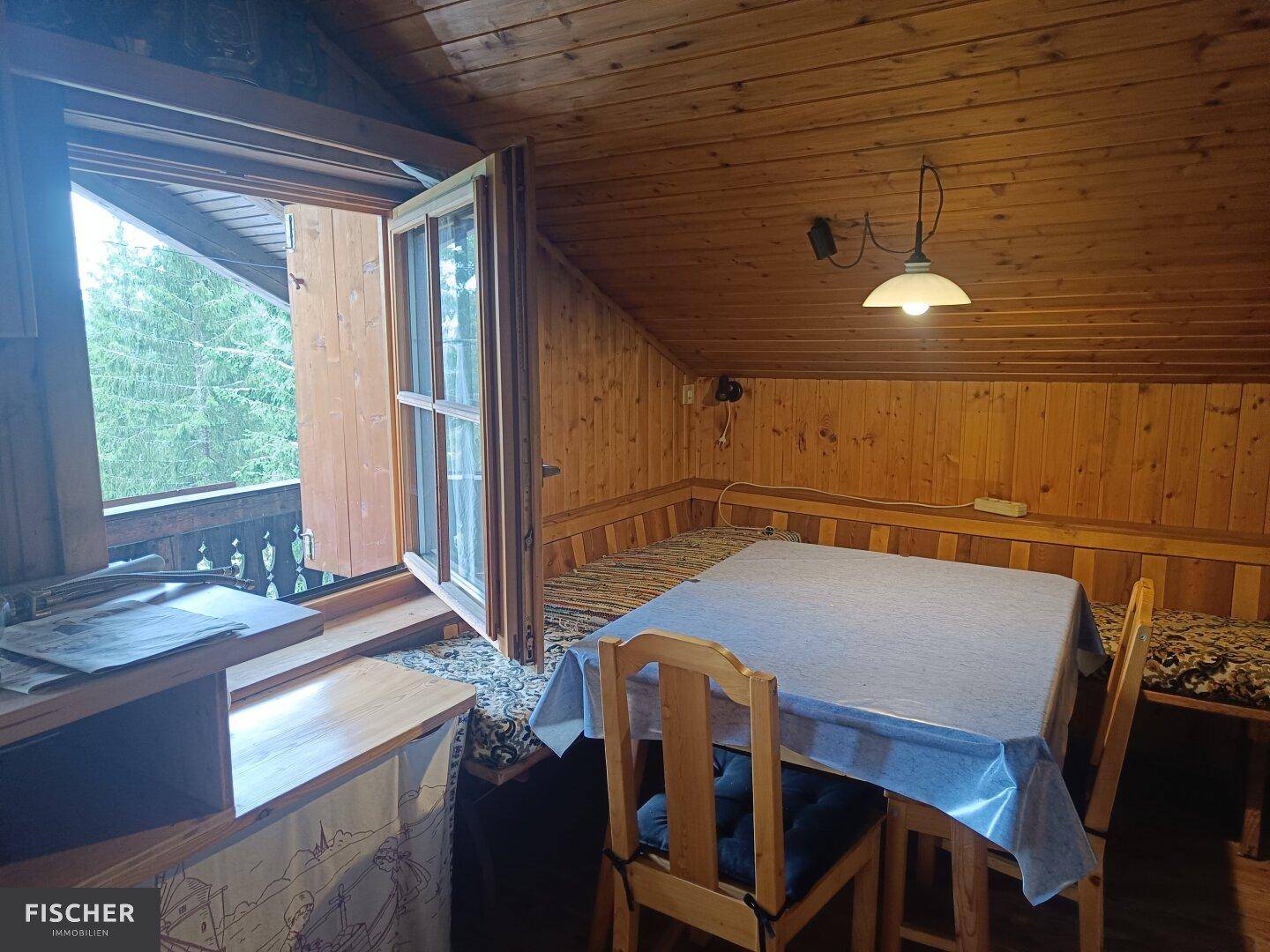 Gemütlicher Essbereich mit Holztisch und Bank, Fenster zum Balkon mit Waldblick.