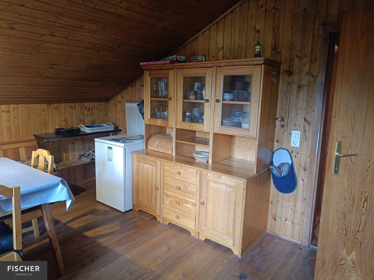 Rustikaler Essbereich im Dachgeschoss mit Holzvertäfelung, traditionellen Möbeln und kleinem Kühlschrank.
