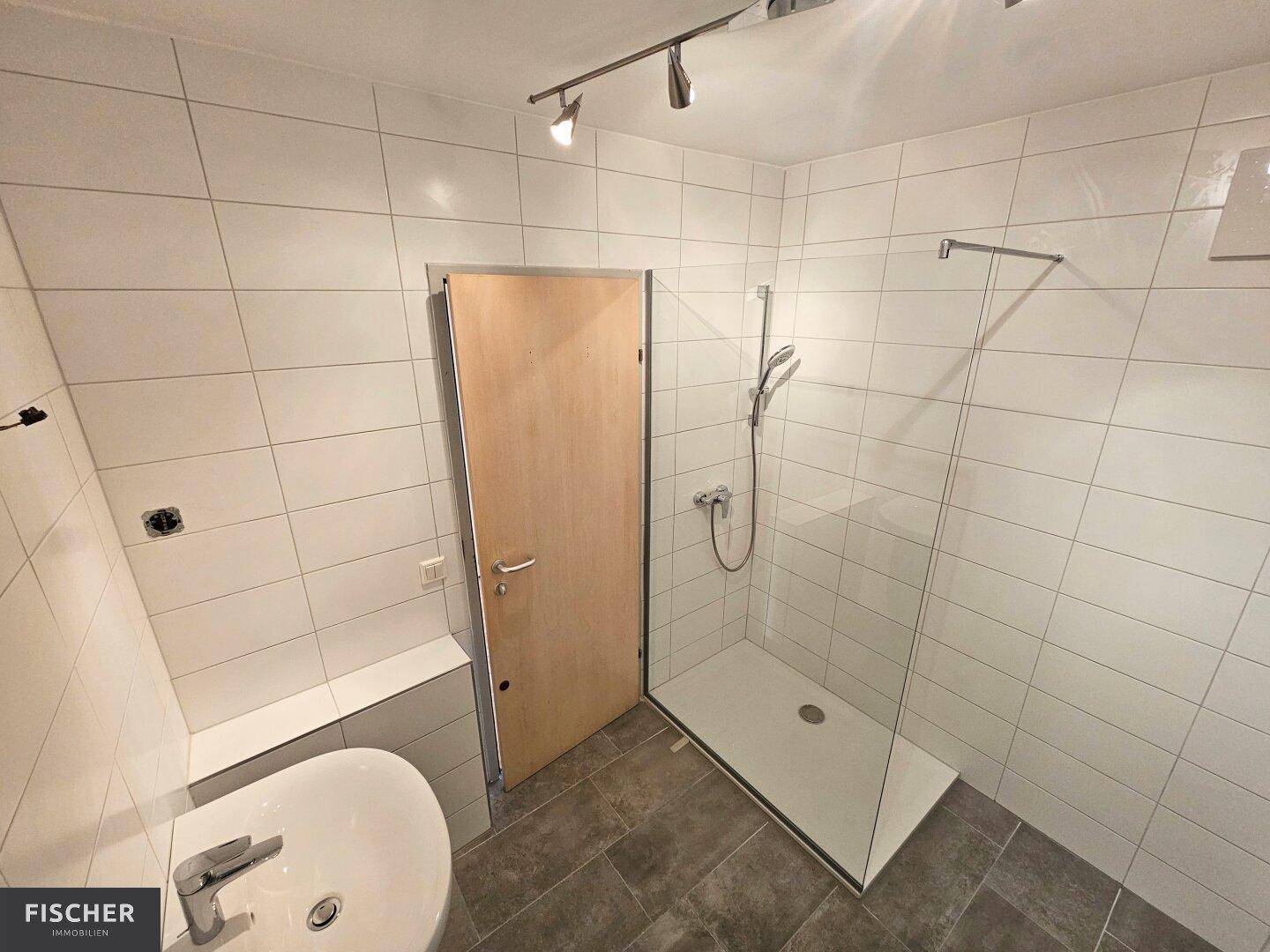 Modern gefliestes Badezimmer mit ebenerdiger Dusche, Glasabtrennung und einem Waschbecken.
