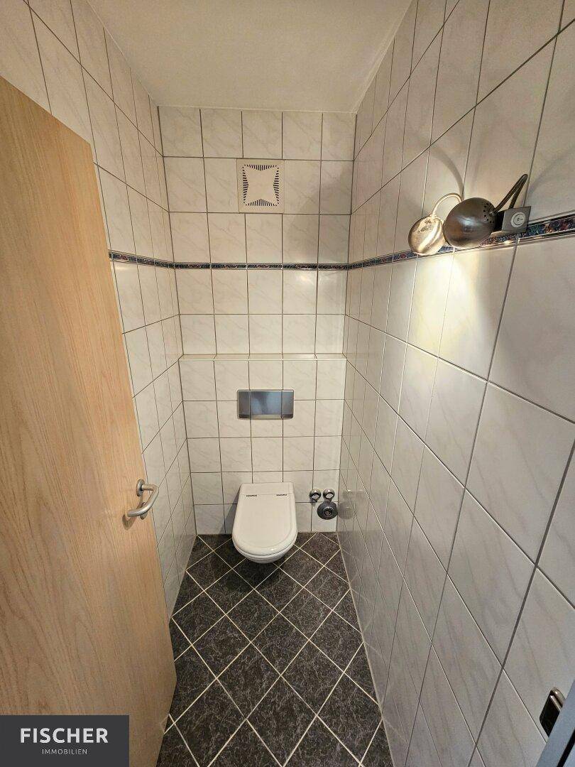 Separates WC mit Wand-WC und Fliesen an Wänden und Boden, praktisch und sauber.