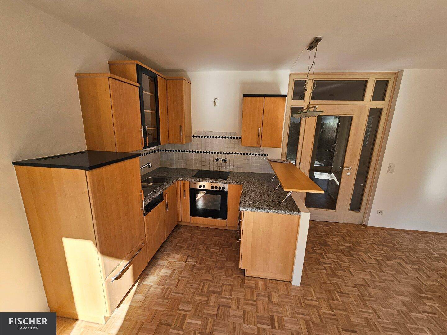Funktionale Einbauküche mit Holzschränken, Kochfeld und Backofen im offenen Wohnbereich integriert.