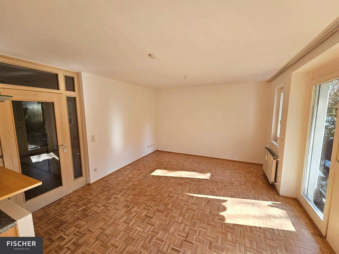 Geräumiges Wohnzimmer mit Parkettboden und viel Tageslicht durch große Fenster und Terrassentüren.