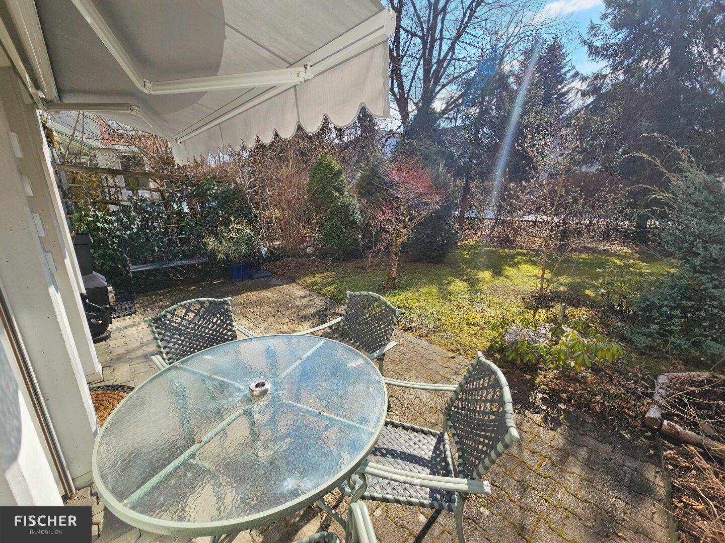 Gemütliche Terrasse mit Esstisch im Freien, umgeben von einem gepflegten Garten mit Bäumen.