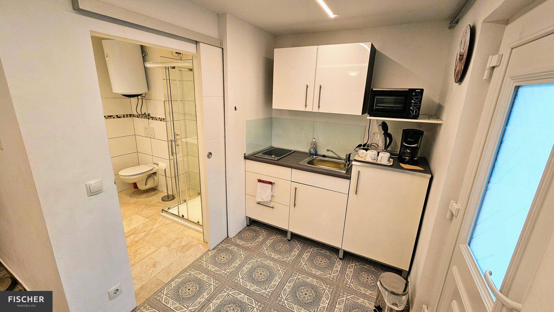 Kleine Küchenzeile mit Spüle, Mikrowelle und Kühlschrank, angrenzend an ein Duschbad.