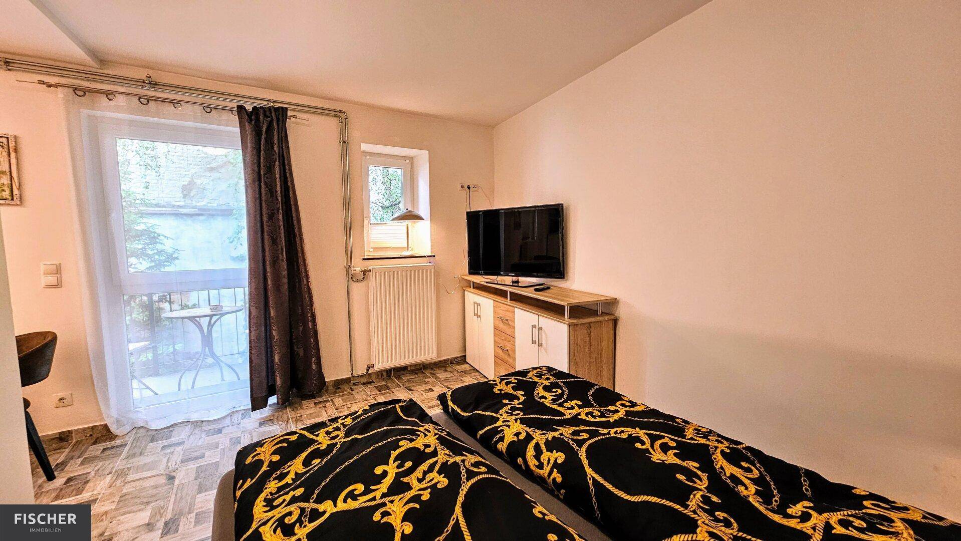 Schlafzimmer mit Doppelbett, Fernseher und direktem Zugang zu einem kleinen Balkon.