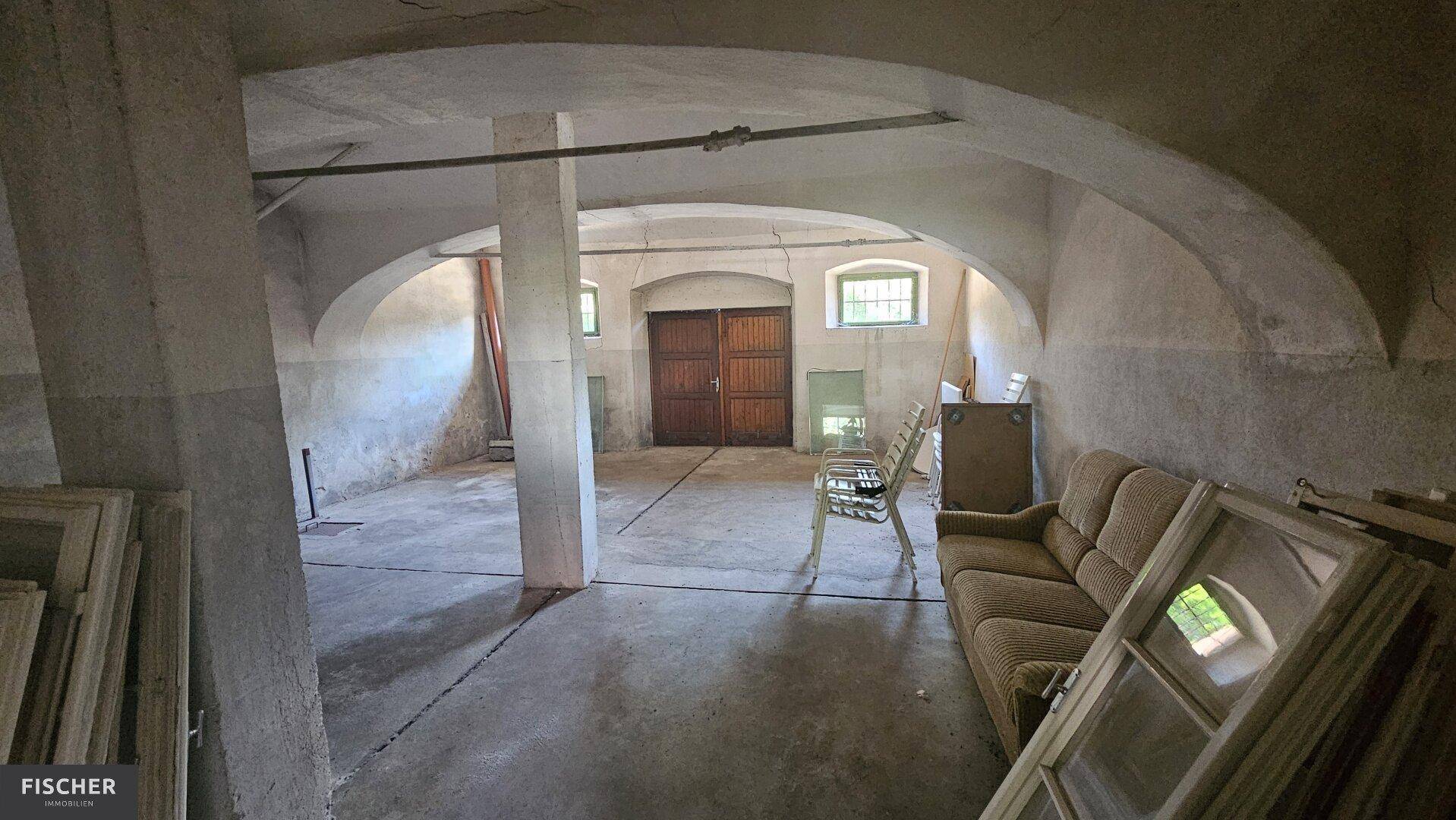 Großer Kellerraum mit Betonboden, gewölbten Decken und alten Holztüren, als Lager genutzt.
