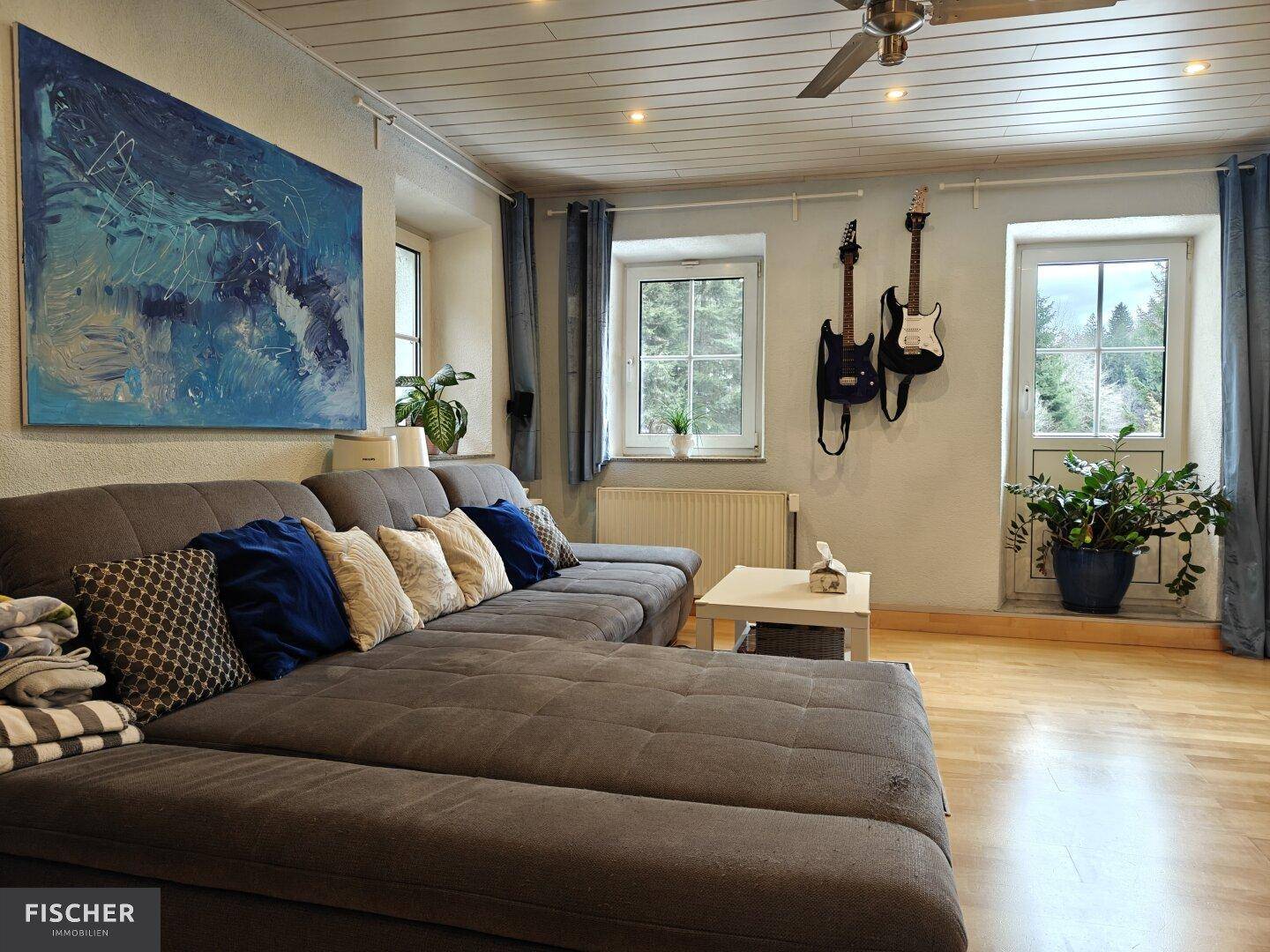 Gemütliches Wohnzimmer mit großem Sofa, Holzboden und Blick in die Natur.