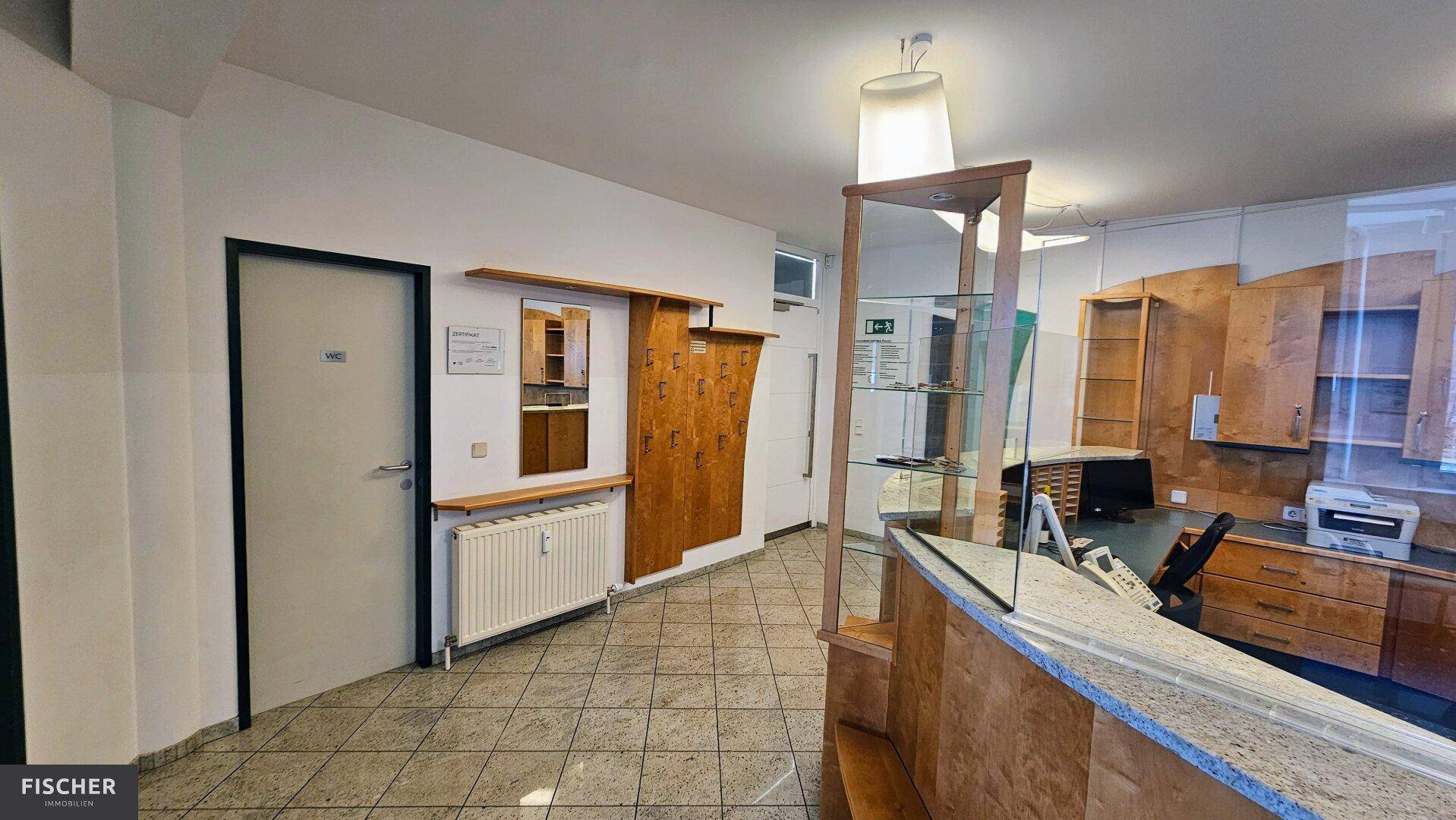 Flurbereich mit Fliesenboden, Garderobe und Zugang zu weiteren Räumen, inklusive einer Glastür.