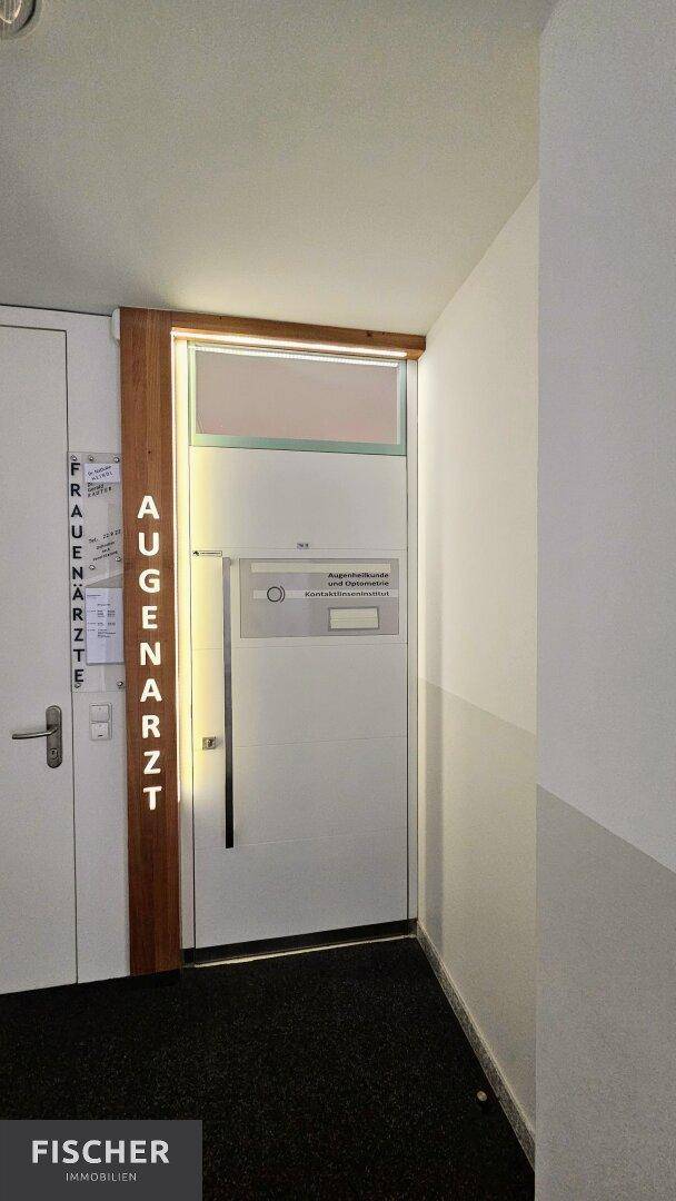 Eingangstür zu einer Augenarztpraxis mit Beschilderung und Holzverkleidung im Flurbereich.