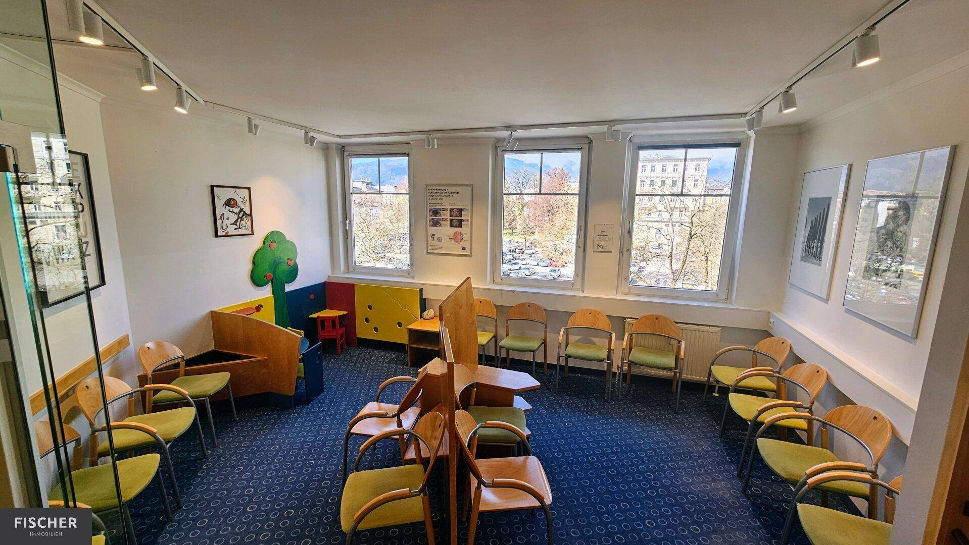Heller Wartebereich mit mehreren Sitzgelegenheiten, Kinderspielecke und Blick auf die Umgebung durch große Fenster.