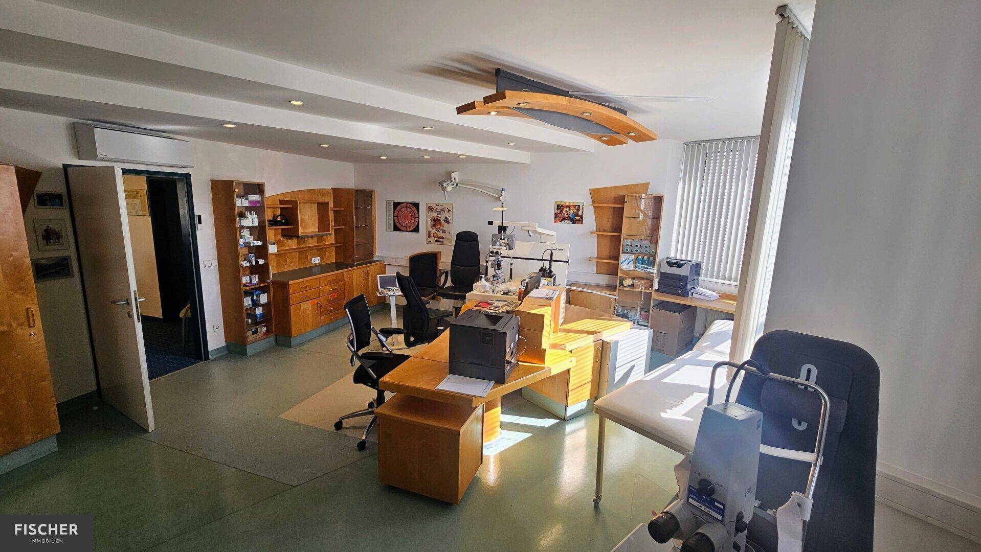Behandlungszimmer mit medizinischen Geräten, Holzmöbeln und Klimaanlage an der Wand in einer Praxis.