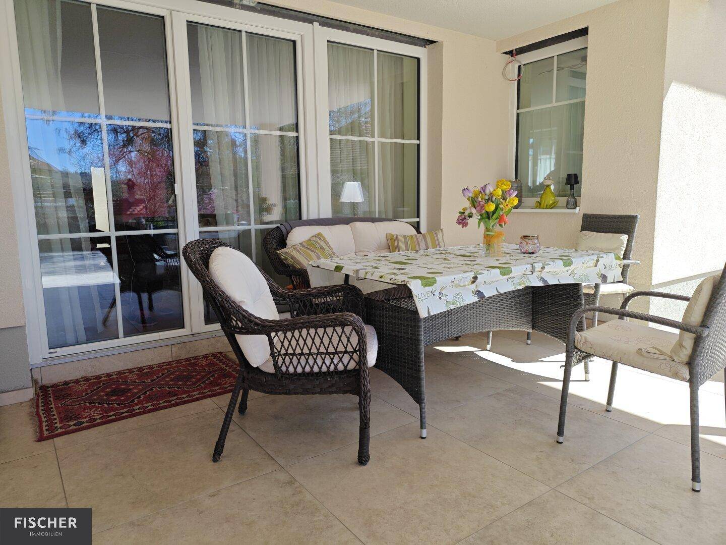 Helle, überdachte Terrasse mit Rattanmöbeln, Esstisch und Zugang zum Innenbereich.