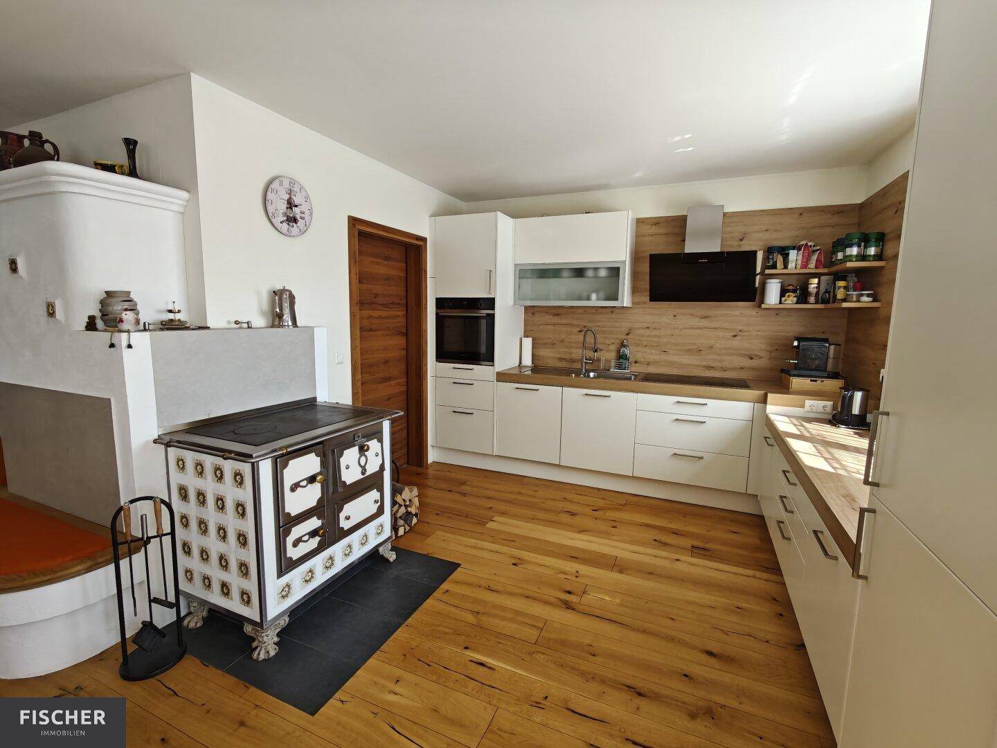 Moderne Küche mit Holzboden, weißen Schränken und traditionellem Holzofen.