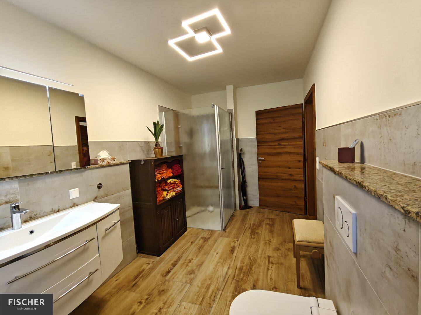 Modernes Badezimmer mit Holzoptikfliesen, Granitwaschtisch und begehbarer Dusche.