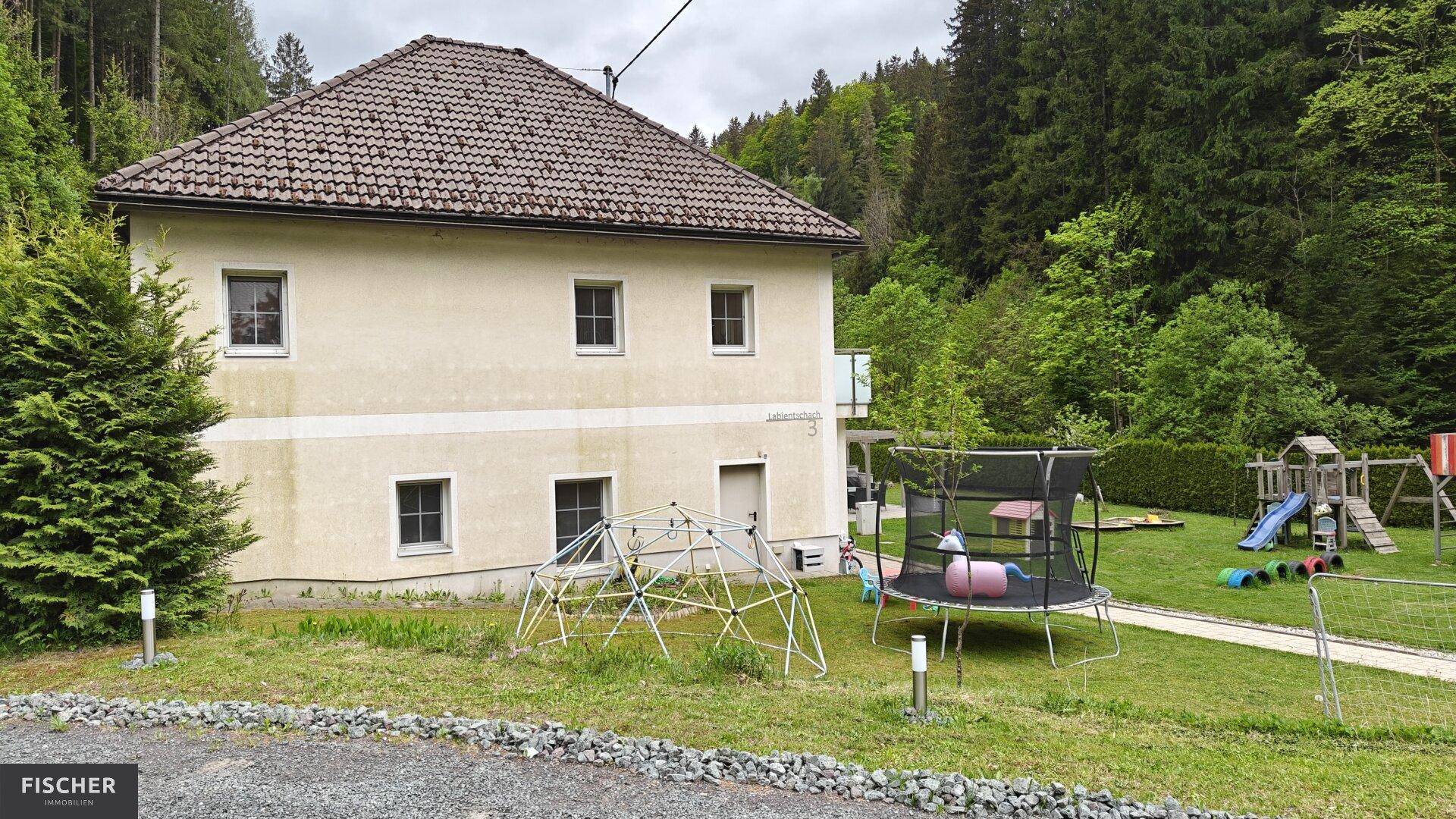 Rückseite des Hauses mit weitläufigem Garten und verschiedenen Spielgeräten für Kinder.