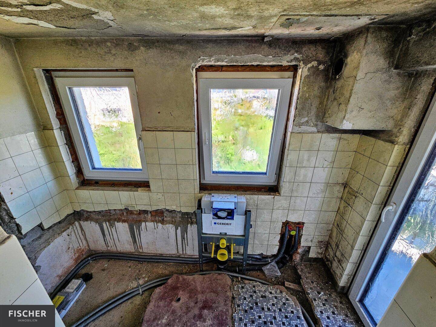 Badezimmer im Rohbau mit neuen Fenstern und vorbereiteten Installationen für WC und Dusche.