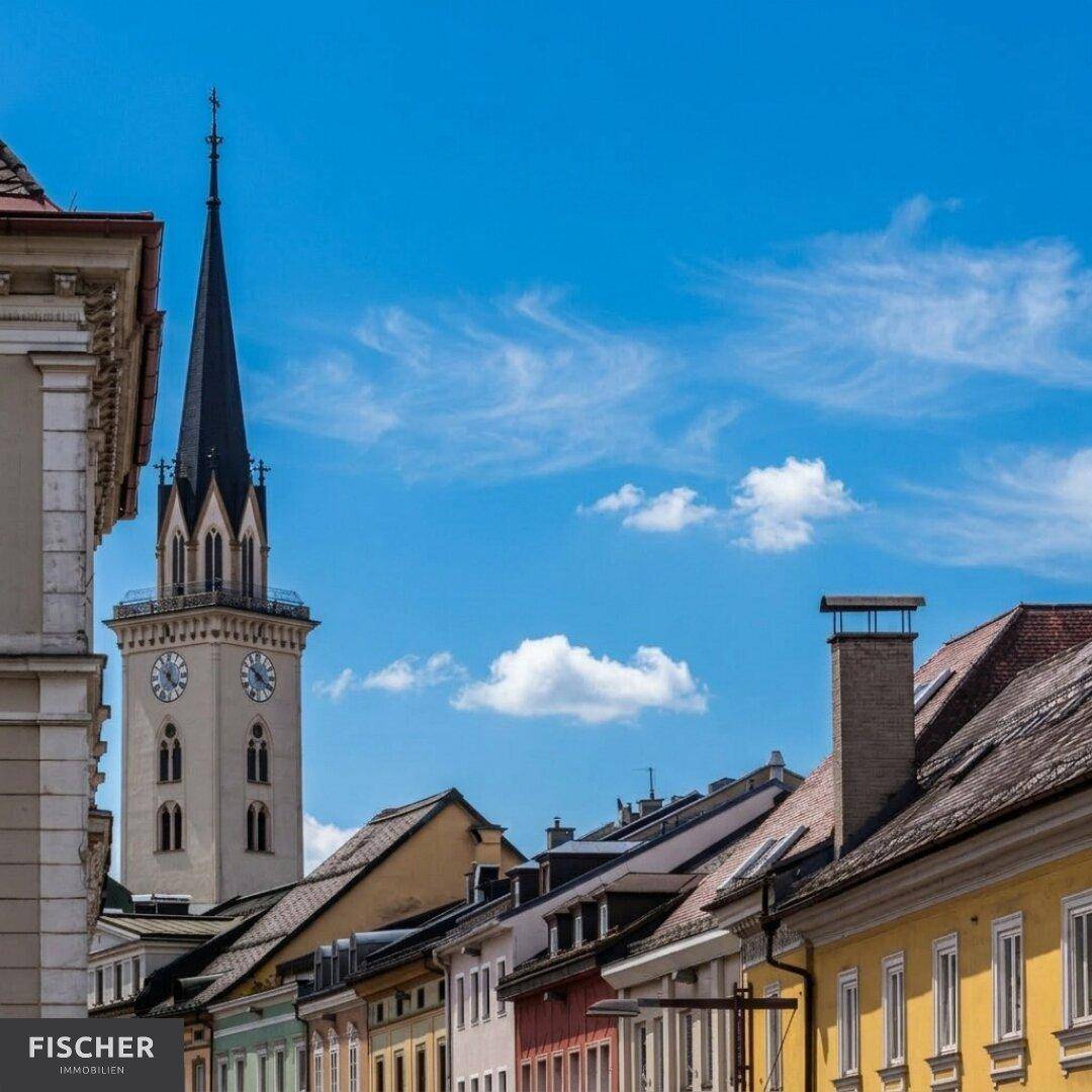 Historische Gebäude mit farbenfrohen Fassaden und einem markanten Kirchturm unter strahlend blauem Himmel.