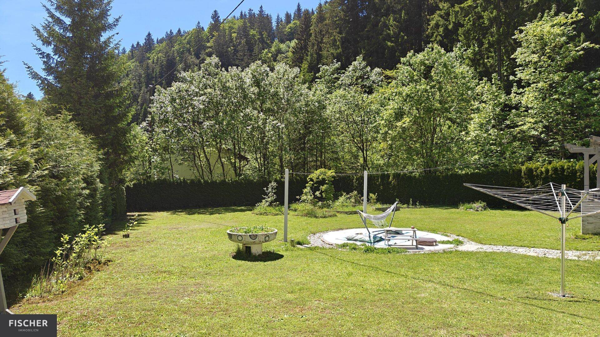Großer, gepflegter Garten mit Hängematte und Wäscheleine, umgeben von Bäumen.