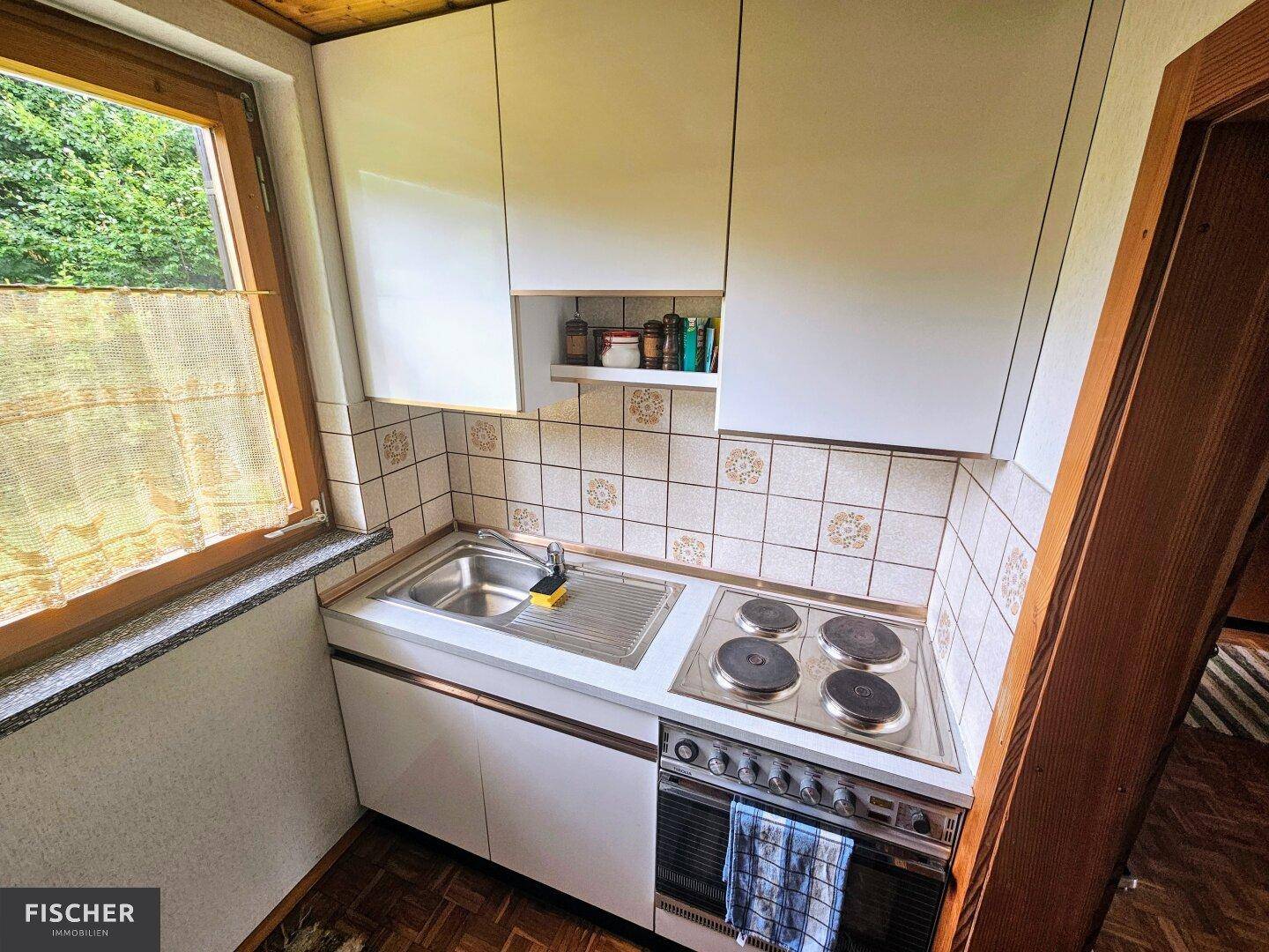 Kleine, funktionale Küche mit weißen Schränken, Elektroherd und Fenster zum Garten.
