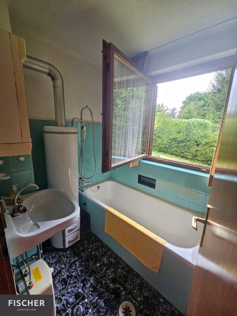 Badezimmer im 80er-Jahre-Stil mit blauen Fliesen, Badewanne und Fenster mit Ausblick.