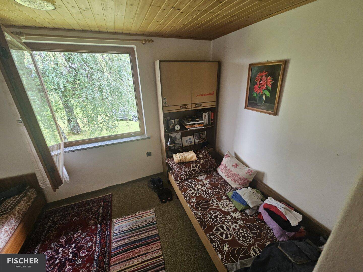 Einfaches Schlafzimmer mit Einzelbetten, Teppichboden und großem Fenster mit Grünblick.