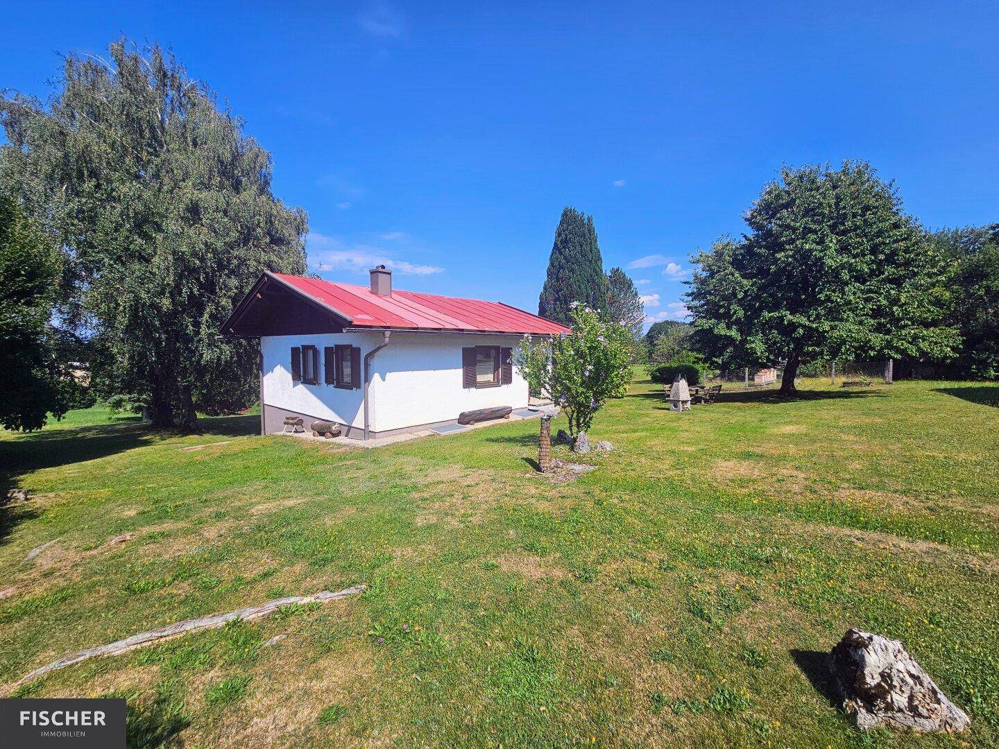 Freistehendes Haus mit rotem Dach inmitten einer weitläufigen grünen Landschaft unter blauem Himmel.