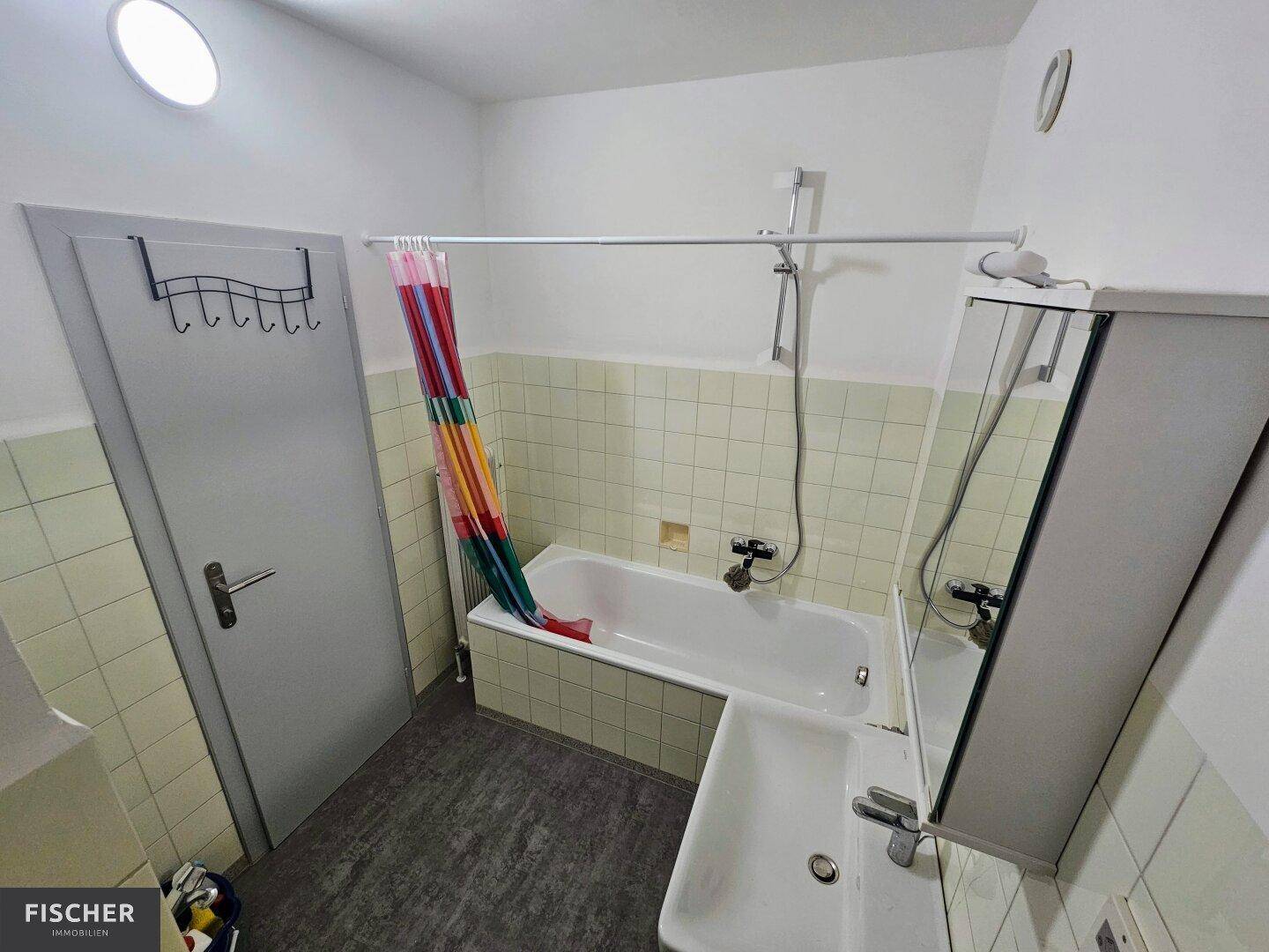 Badezimmer mit Badewanne, Waschbecken und hellgrünen Fliesen, ausgestattet mit Spiegelschrank.