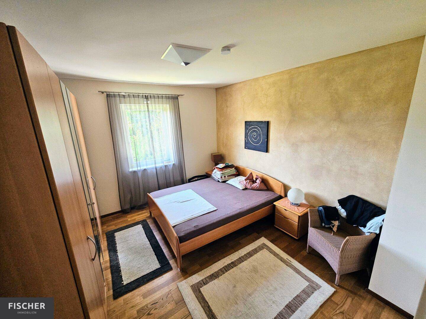 Schlafzimmer mit Holzboden, großem Kleiderschrank und Fenster mit Blick ins Grüne.