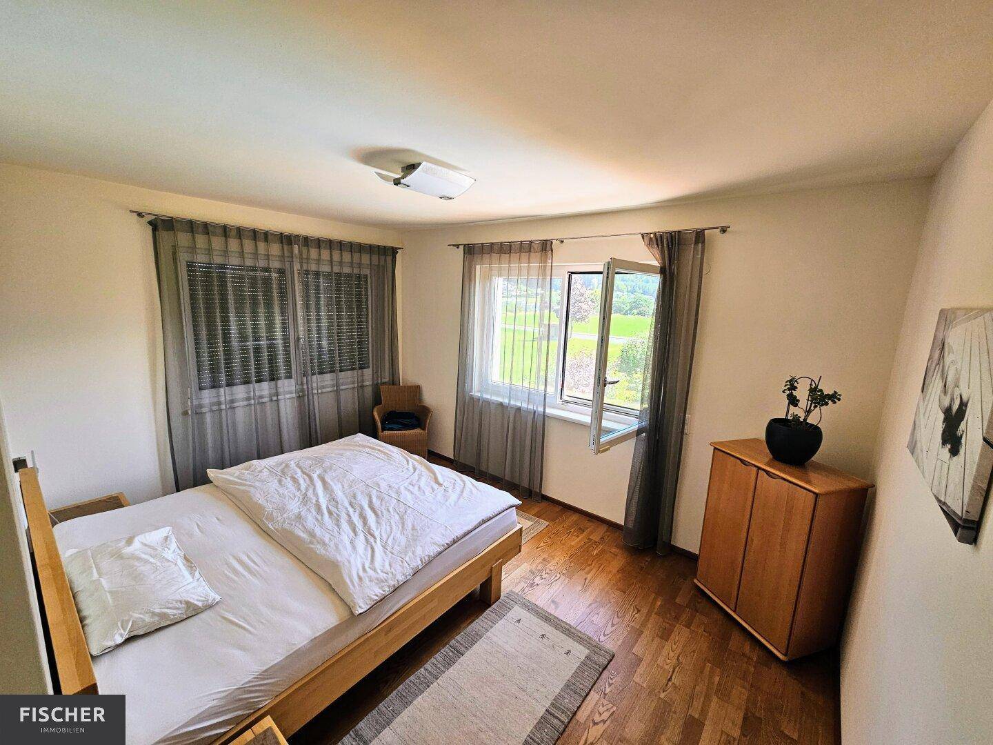 Schlafzimmer mit Holzboden, Fenster und Vorhängen, bietet eine ruhige Atmosphäre.