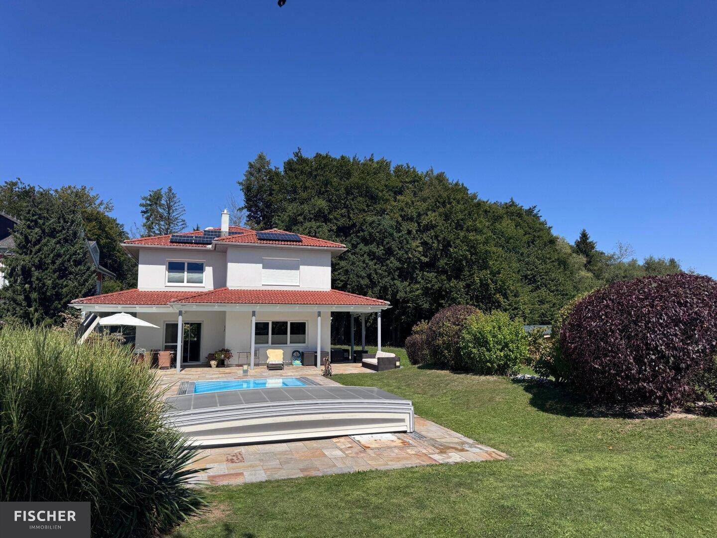Weitläufiger Gartenbereich mit Pool, Einfamilienhaus und üppiger Vegetation unter blauem Himmel.