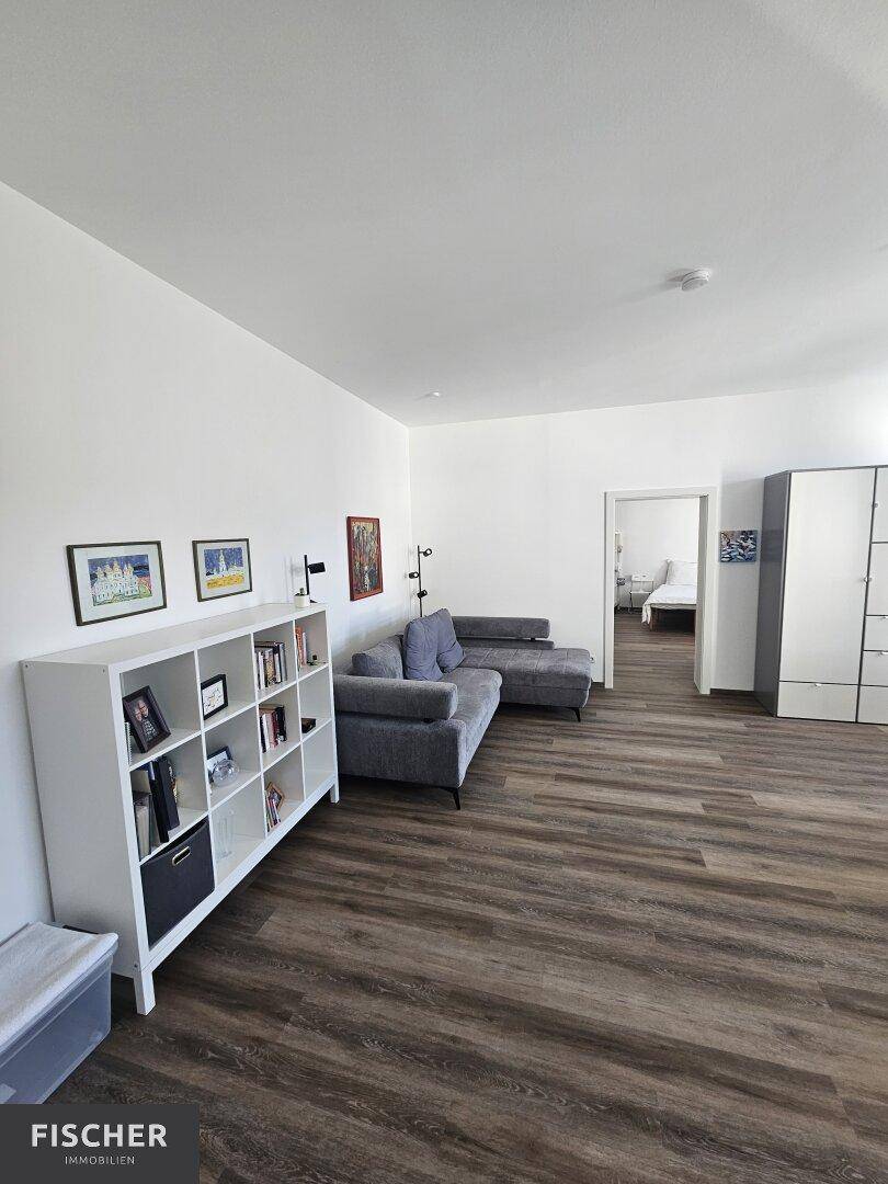 Gemütlicher Wohnbereich mit grauem Ecksofa und weißem Bücherregal.