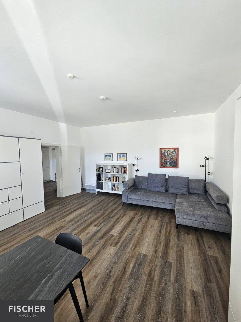 Heller Wohn- und Essbereich mit grauem Sofa und dunklem Esstisch.