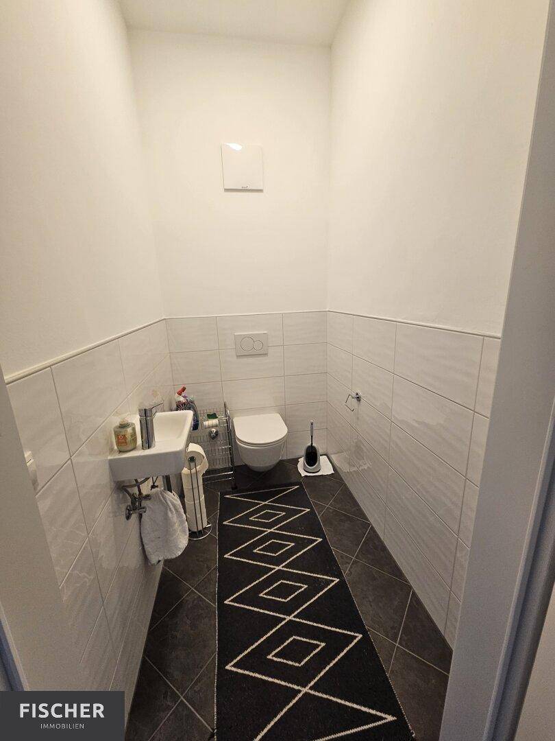Kleines Gäste-WC mit Wand-WC, Waschbecken und dunklen Bodenfliesen.